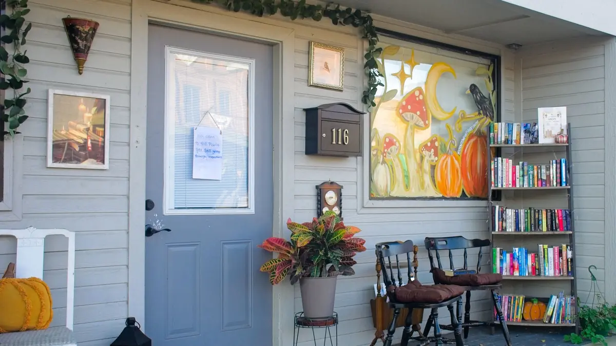 Small-town storefront entrance with a bookshelf, potted plants, and porch chairs