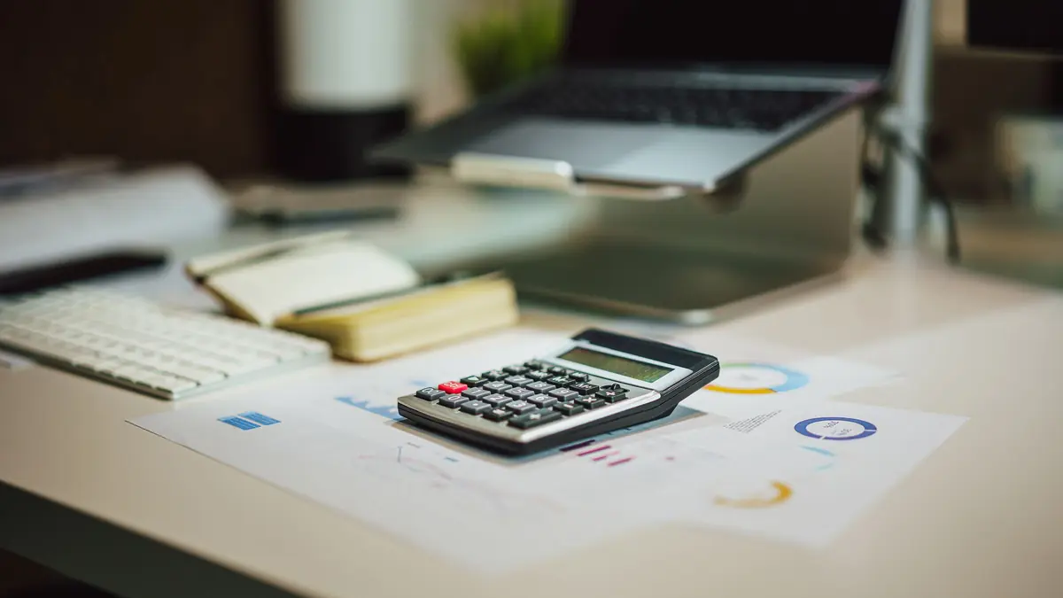 Desk with a calculator, laptop, and printed financial documents