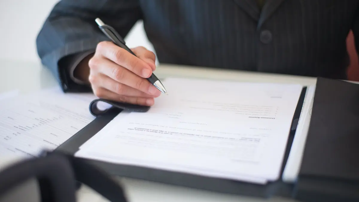 Person in a suit signing business documents in a folder at a desk